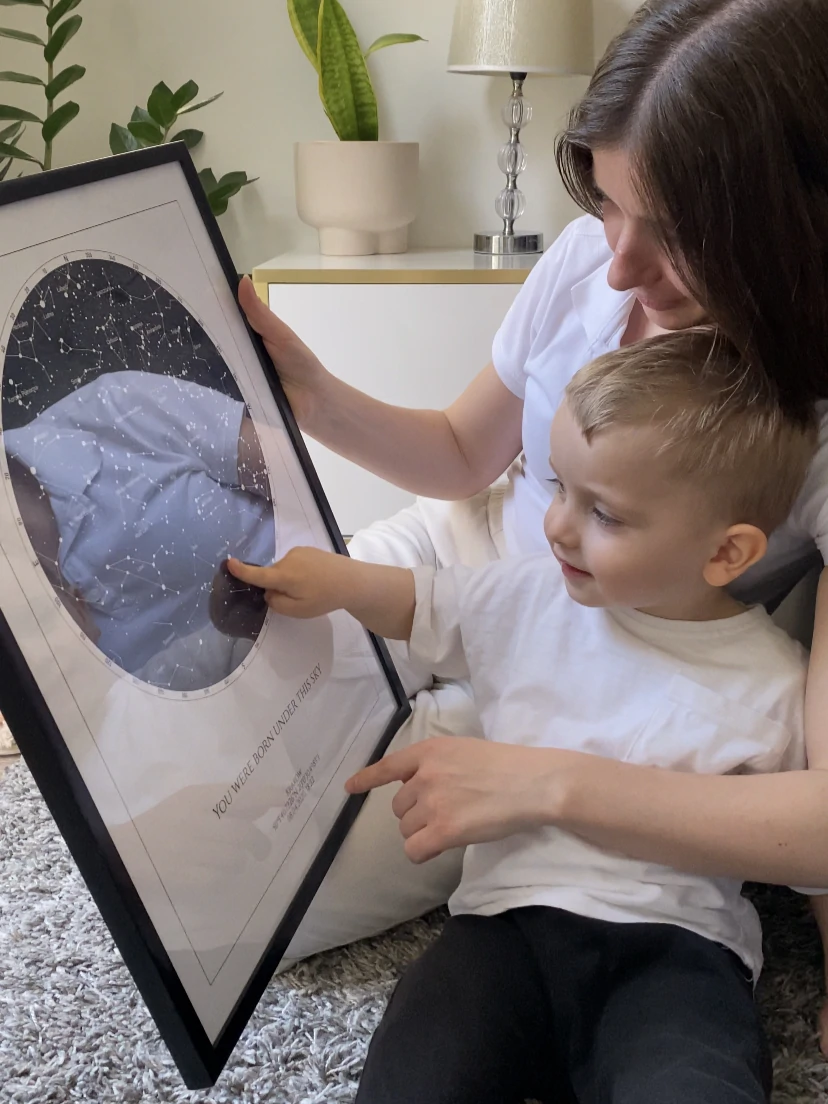 Maminka s chlapečkem si prohlížejí zarámovanou hvězdnou mapu k narození dítěte.
