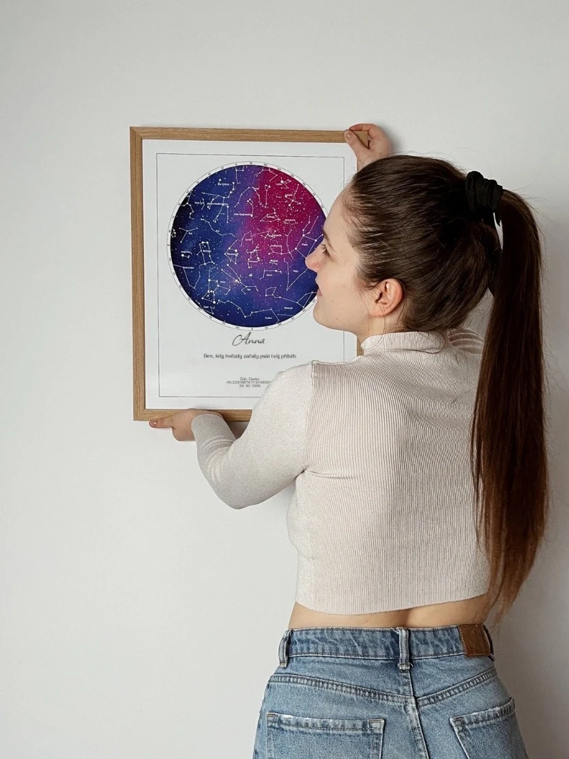 Žena v bílém svetru drží originální dárek – hvězdnou mapu podle narození.